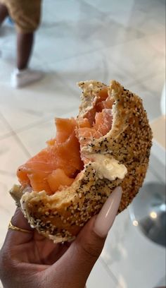 someone is holding up a bagel with salmon and sesame seeds on it in their hand