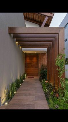 an entrance to a modern home with wood and plants on the side walk leading up to it