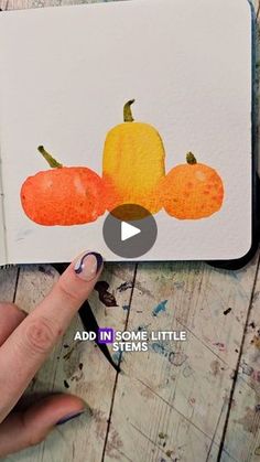 a hand holding a pen next to an open notebook with watercolor pumpkins on it