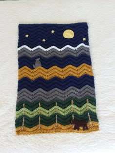 there is a crocheted blanket on the bed with a bear and moon in the sky