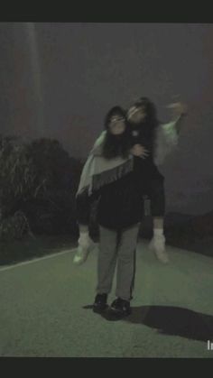 two people standing in the middle of a road at night with their arms around each other