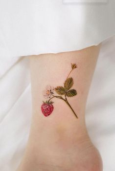 a small strawberry tattoo on the ankle with leaves and flowers attached to it's side