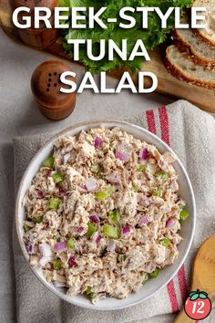 a white bowl filled with tuna salad on top of a table next to sliced bread