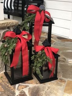 two black lanterns with red bows and bells are sitting on the front porch next to a bench