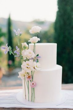 a three tiered white cake with flowers on the top and bottom is sitting on a table