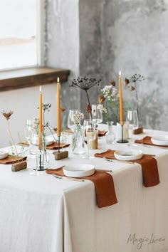 the table is set with white plates and brown napkins, candles, and flowers