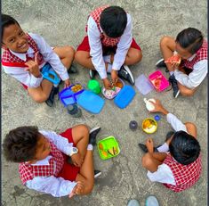 four children are sitting on the ground eating and playing with their lunchbox's