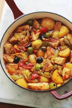 a pot filled with meat and vegetables on top of a counter next to a wooden spoon