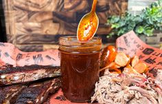 a jar filled with bbq sauce sitting on top of a table next to ribs