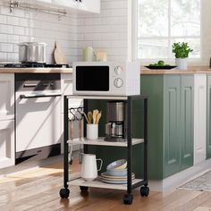 a kitchen with green and white cabinets, wood flooring and a microwave on a cart