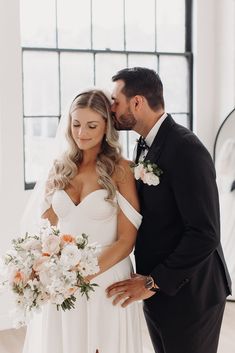 a bride and groom pose for a wedding photo in front of a large window with black framed windows