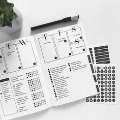 an open planner with black and white stickers on it next to a potted plant