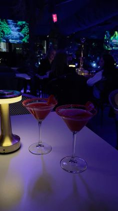 three martini glasses sitting on top of a table in front of a neon light display