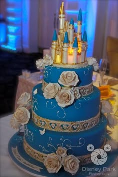 a three tiered blue cake with white roses and gold trimmings on top