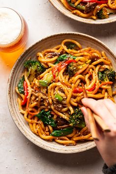 two bowls filled with noodles and vegetables next to a glass of beer