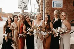 a group of women standing next to each other in front of a brick building holding bouquets