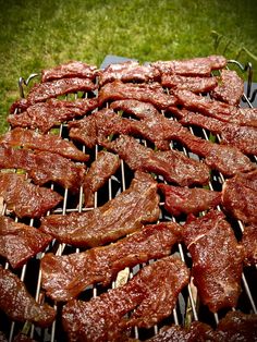 steaks and ribs cooking on a grill in the grass with tongs sticking out