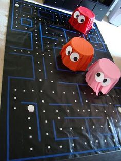 three paper pac - man on a black tablecloth with blue squares and white dots