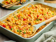 a casserole dish full of pasta and peas with a wooden spoon in it