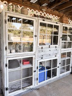 an old white china cabinet with glass doors and windows on the top, in front of a wooden wall