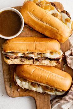 three sandwiches with meat, cheese and sauce on a cutting board