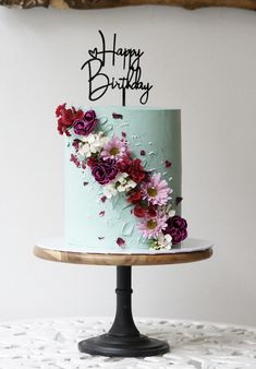 a blue birthday cake with pink and purple flowers on it, sitting on a table