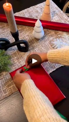 a person cutting out a piece of paper with scissors and a candle on the table