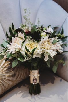 a bridal bouquet sitting on the back of a chair with greenery and flowers