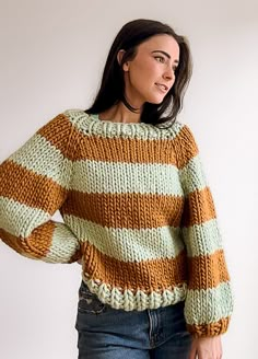 a woman standing in front of a white wall wearing a sweater with stripes on it