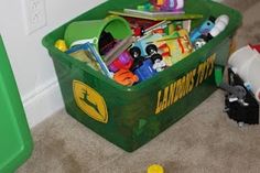 a green bin filled with lots of toys next to a toy truck on the floor