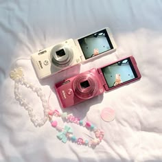 two cameras sitting next to each other on top of a white sheet with beaded necklaces