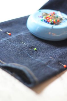 a blue piece of cloth with pins on it and a small button in the middle