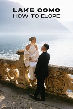 a man standing next to a woman on top of a stone wall near the ocean