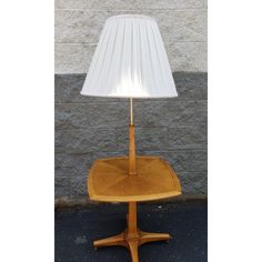 a wooden table lamp with a white shade on it's base and a brick wall in the background