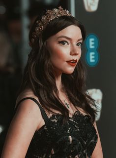 a woman in a black dress with a gold crown on her head and dark lipstick