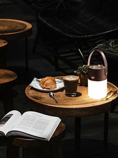 a wooden table topped with a plate of food and a cup of coffee next to an open book