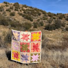 a patchwork quilt sitting on top of a dry grass covered field next to a hill