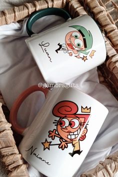 two coffee mugs with cartoon characters on them sitting in a wicker basket next to each other