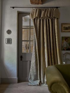 a living room with a green couch and striped curtains on the window sill, in front of a white door