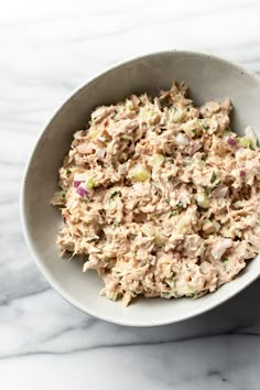 a white bowl filled with tuna salad on top of a marble counter next to a fork