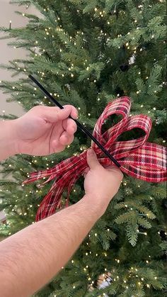 a person holding scissors near a christmas tree with red and white ribbon on it's bow