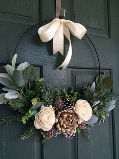 a wreath with flowers and pine cones hanging on a door hanger that is decorated with greenery