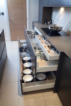 an open drawer in the middle of a kitchen with pots and pans on it