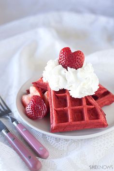 waffles with whipped cream and strawberries on a plate next to utensils