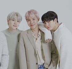 three young men standing next to each other in front of a white wall and wearing beige clothing