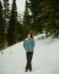 a woman standing in the snow with trees behind her