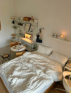 a bed with white sheets and pillows in a bedroom next to a desk, chair and shelves