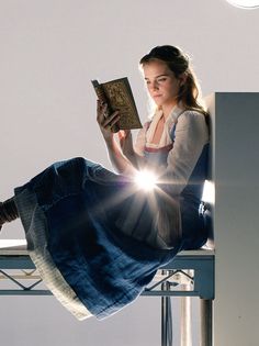 a woman sitting on top of a chair reading a book with the sun shining through her eyes