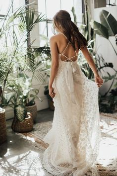 the back of a woman wearing a white dress and standing in front of potted plants