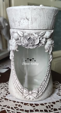 a white vase sitting on top of a lace doily tablecloth covered table next to a window